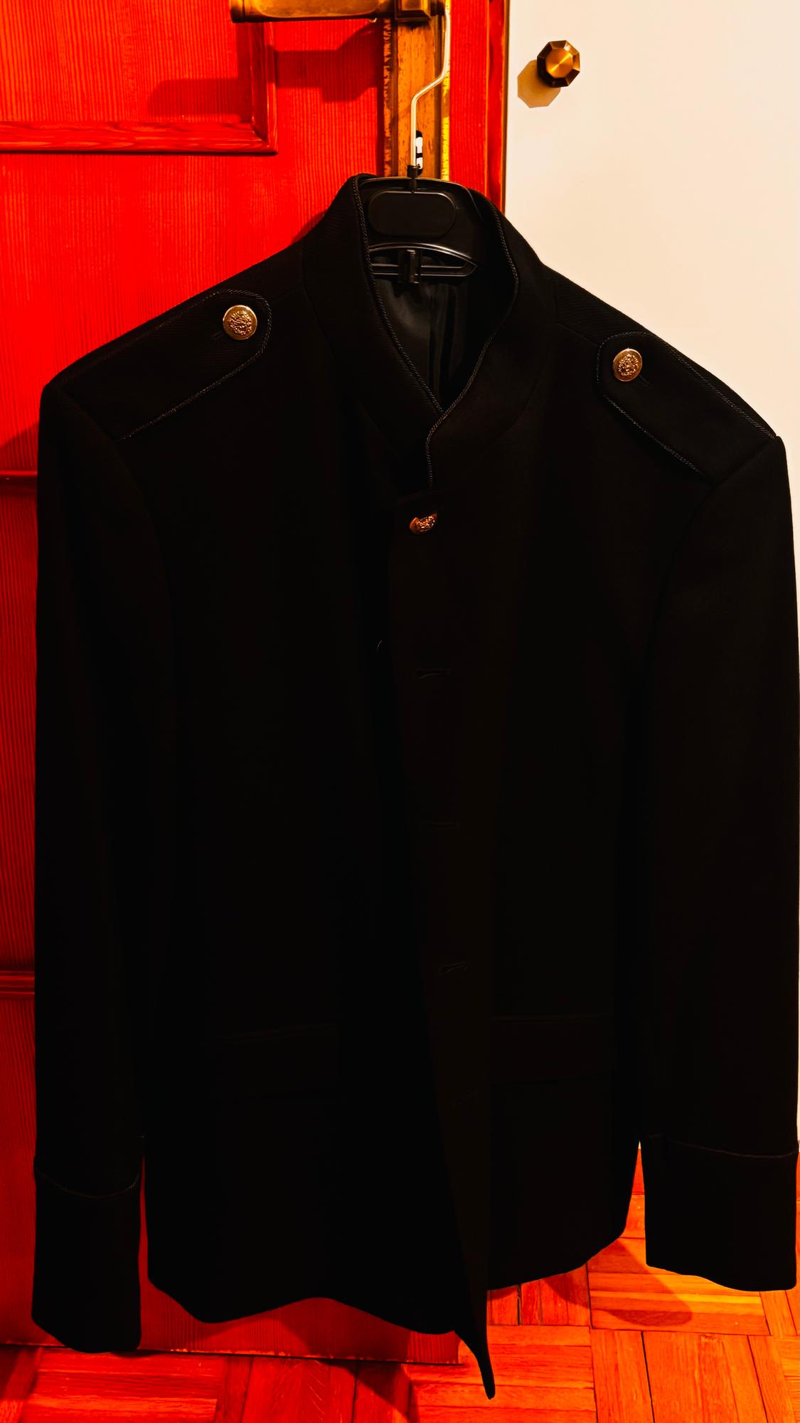 Black jacket with gold buttons on the shoulders, hanging on a red wooden door.