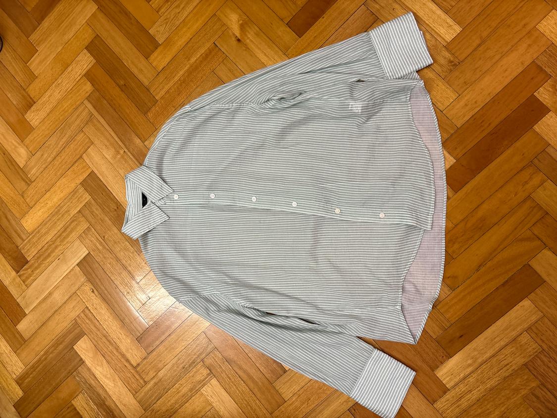 White and grey striped shirt with white buttons, placed on a herringbone wooden floor.