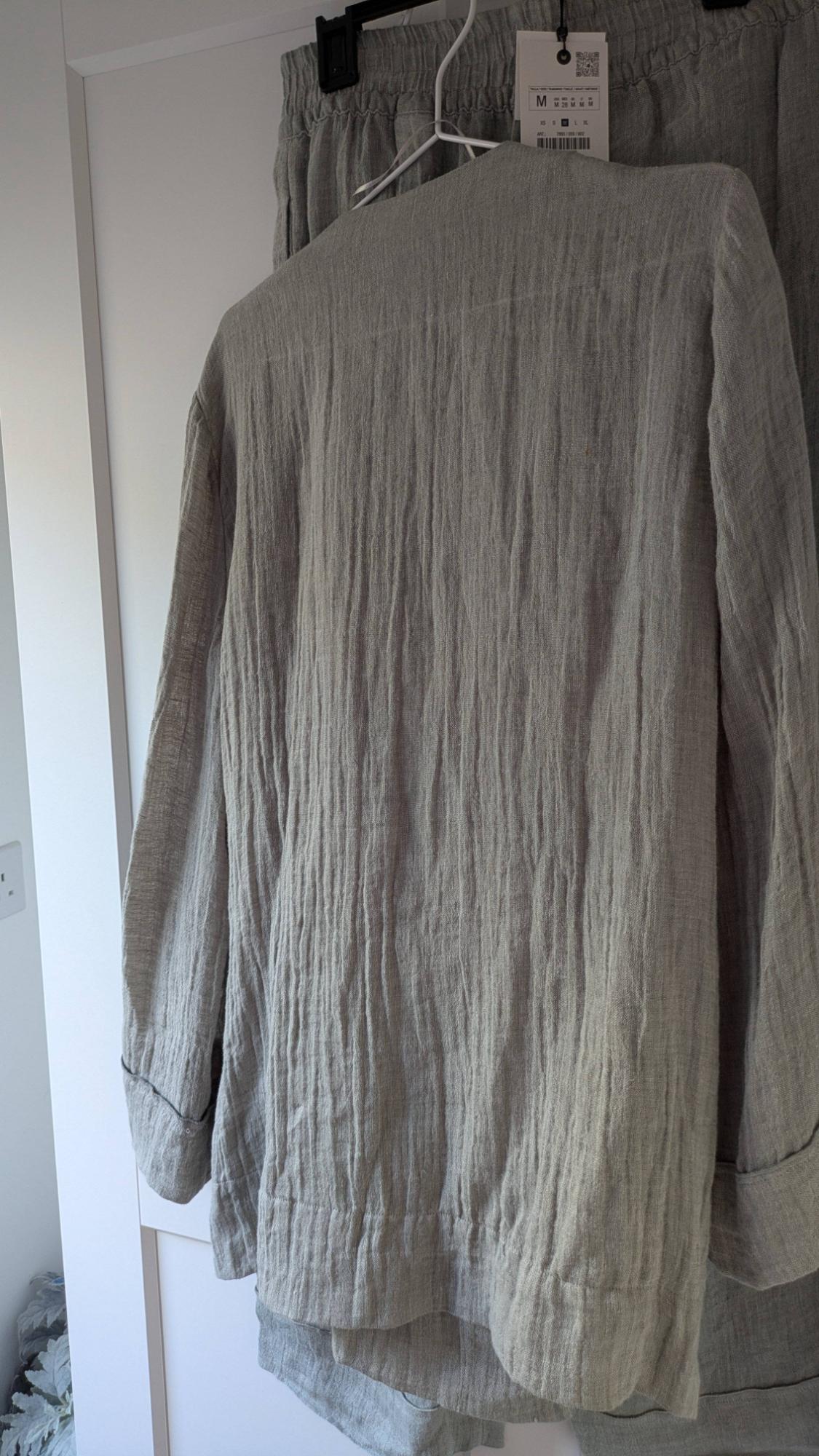 Grey linen crinkle-texture shirt hanging on a hanger, next to matching trousers, in a white wardrobe.