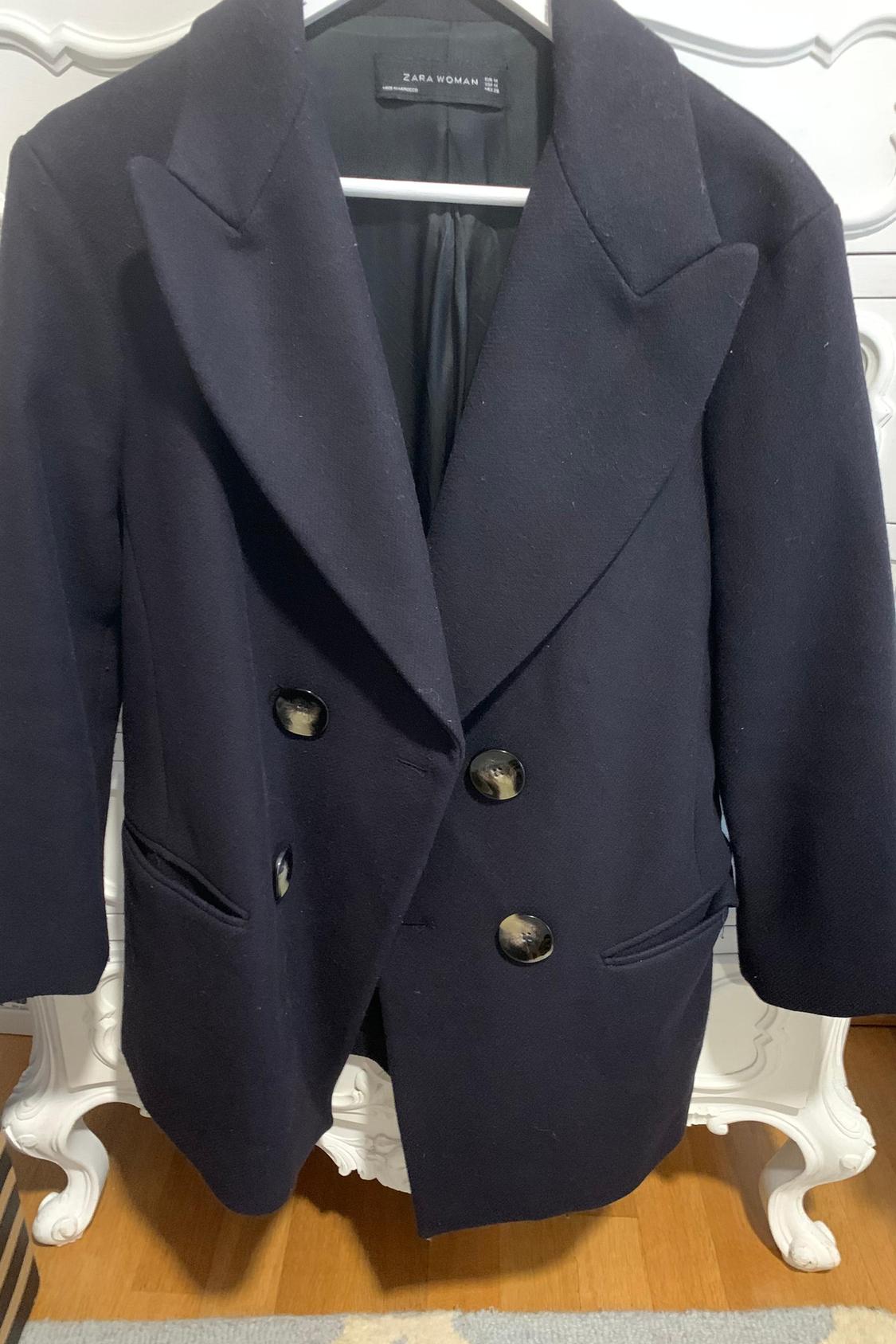 Front view of black coat with wide lapels and large buttons. Visible side pockets.