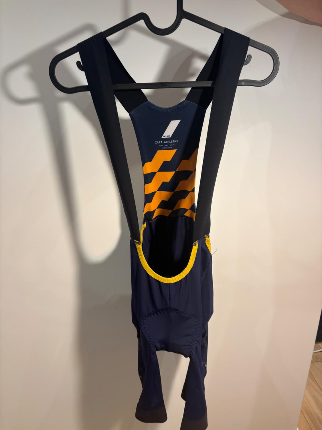 Blue tracksuit with black straps and yellow details, hanging on a hanger. Visible text: "ZARA ATHLETICZ".