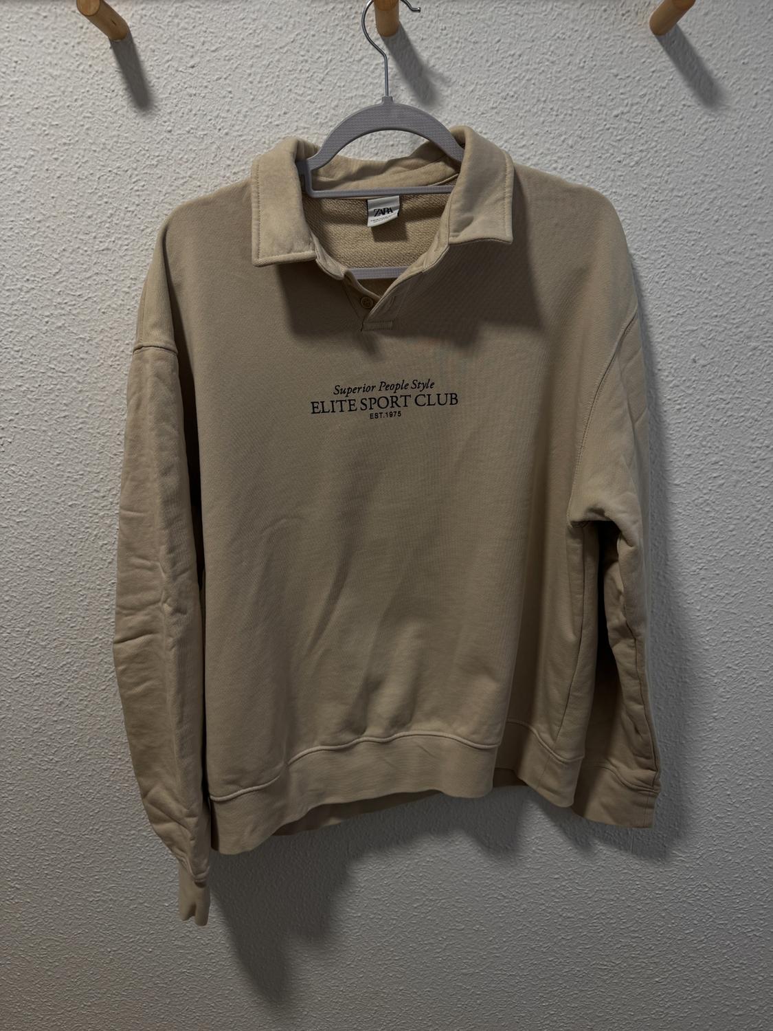 Beige polo neck sweatshirt hanging on a hanger. Text on chest: "Superior People Style ELITE SPORT CLUB EST. 1975".