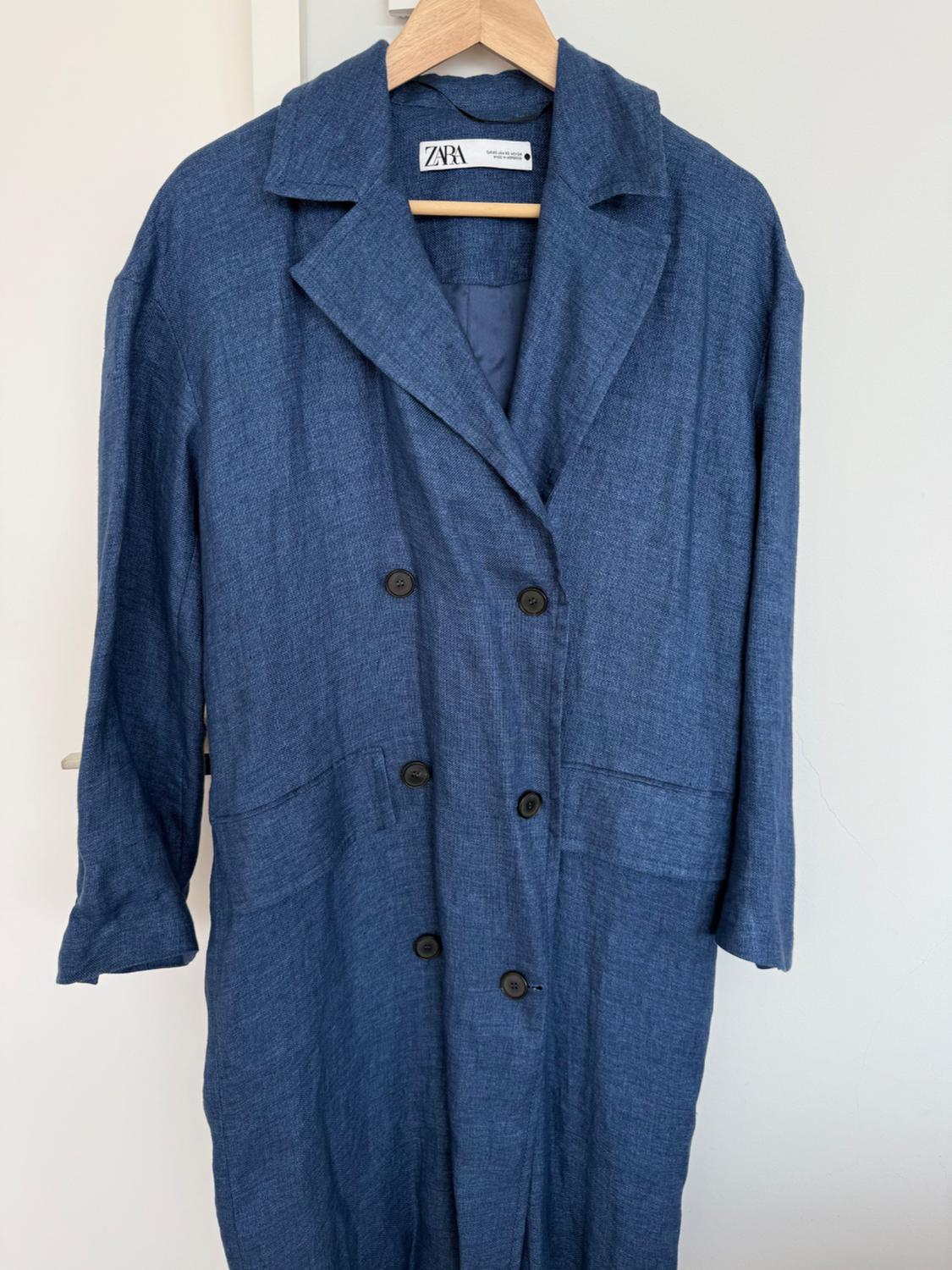 Blue textured fabric double-breasted coat with lapels, hanging on a wooden hanger. Visible label: ZARA.
