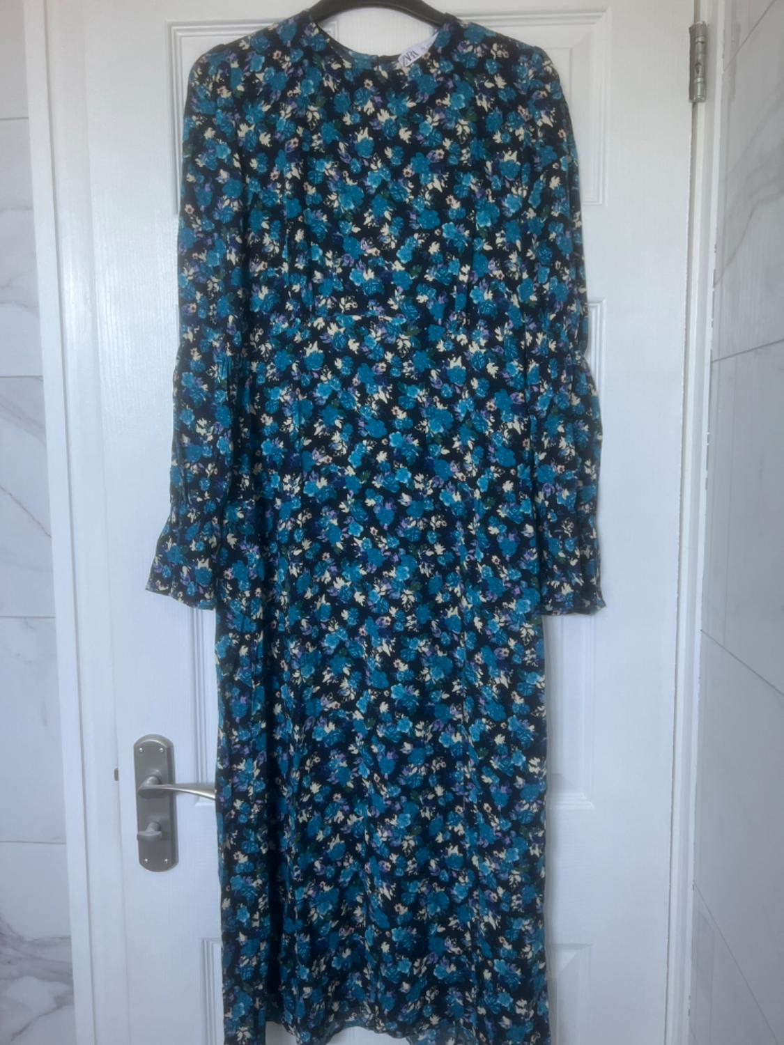 Long dress with a blue and black floral print hanging on a white door. Interior setting with marble walls.