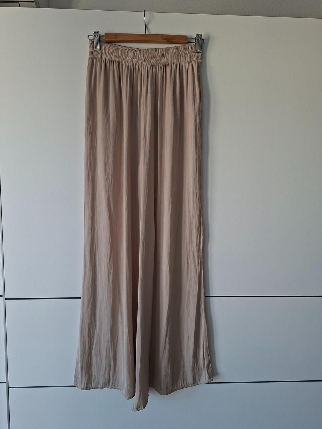 Flowing wide-leg beige trousers with an elasticated waist, hanging on a wooden hanger against a white wardrobe background.