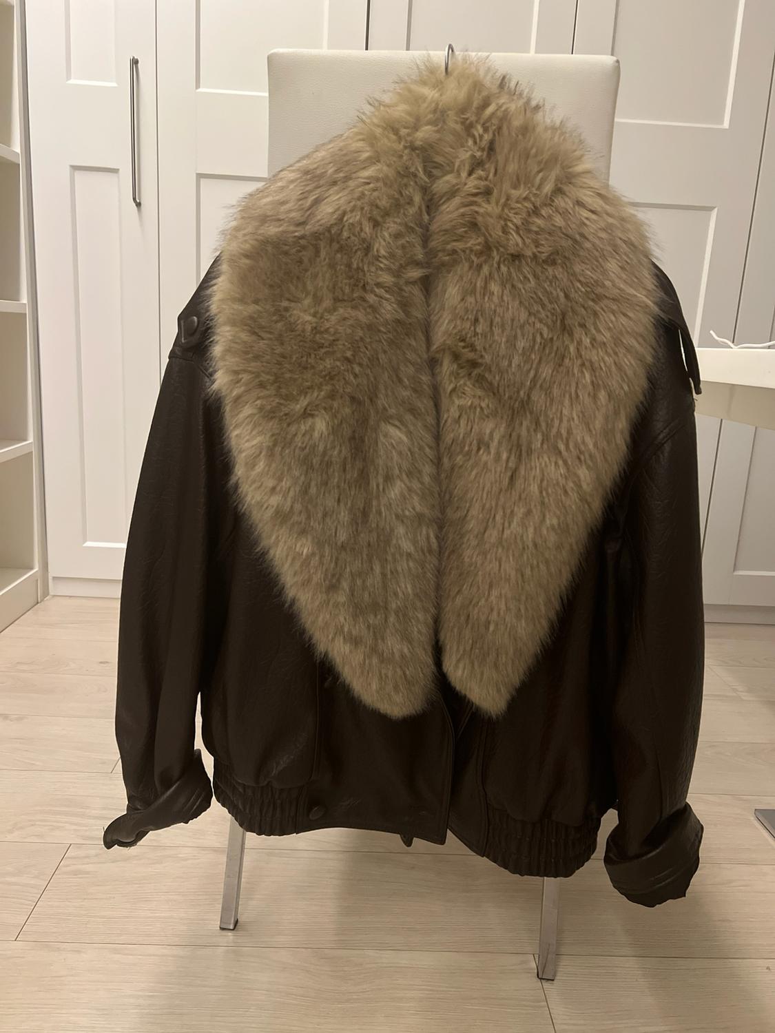 Brown jacket with a large beige fur collar, hanging over a white chair in a room with white wardrobes and a wooden floor.