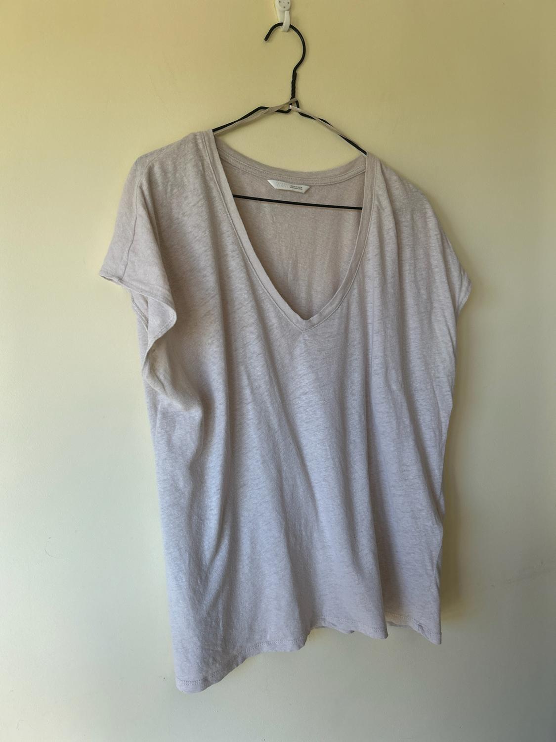 Basic beige short-sleeved V-neck T-shirt hanging on a black wire hanger against a plain cream-coloured wall.
