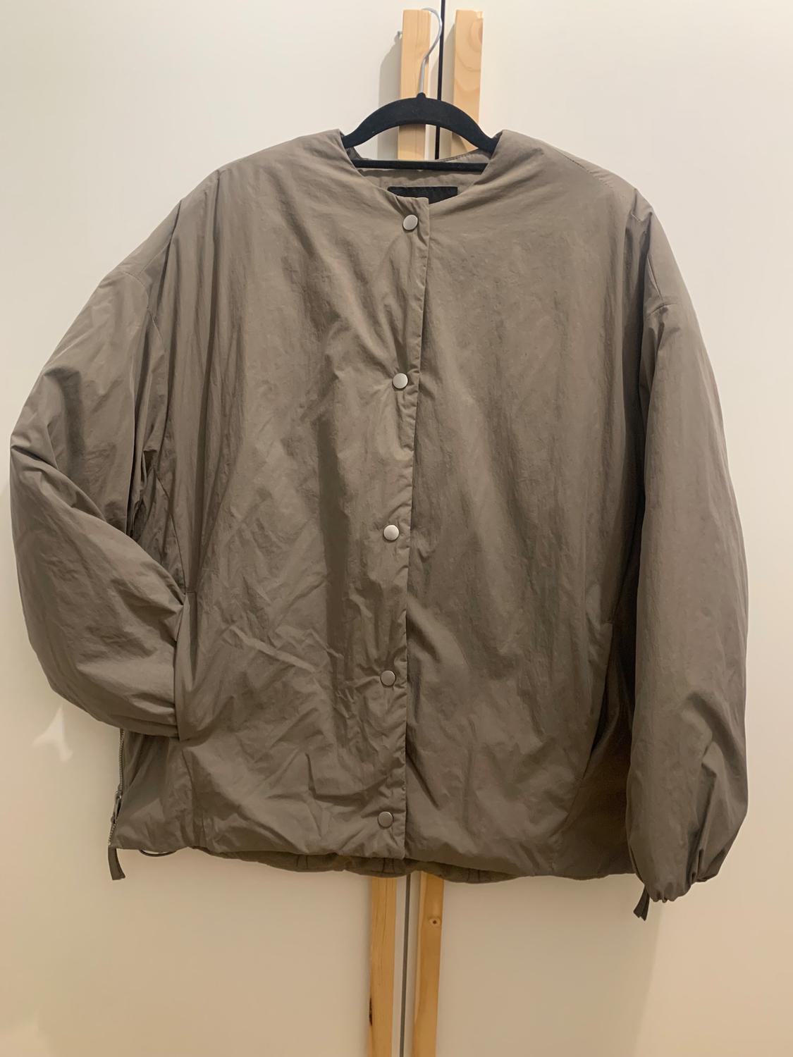 Light brown jacket with front buttons, hanging on a black hanger against a white background.