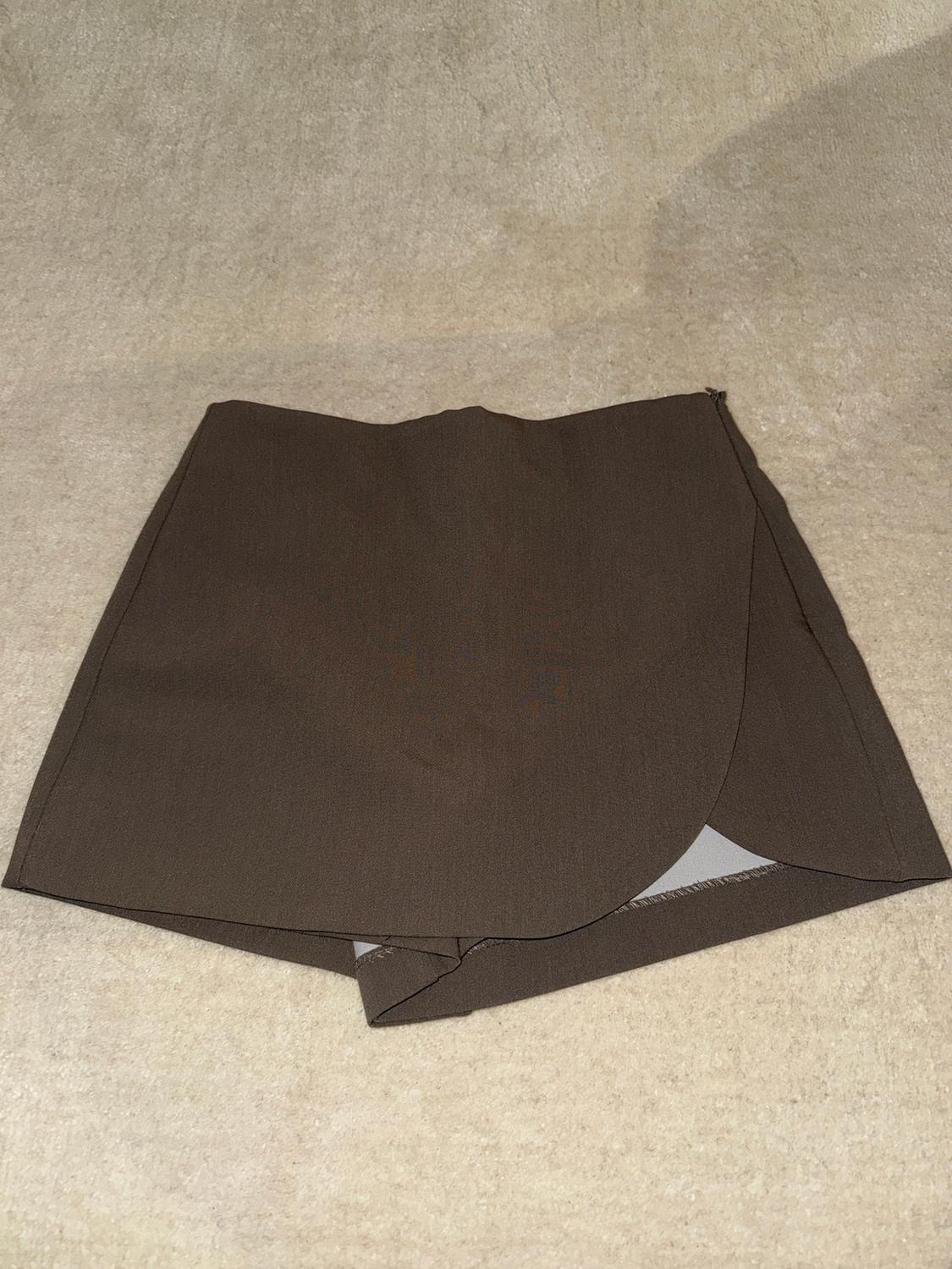 Brown short skirt on a beige background, with a wrap-around design and an asymmetrical hem.