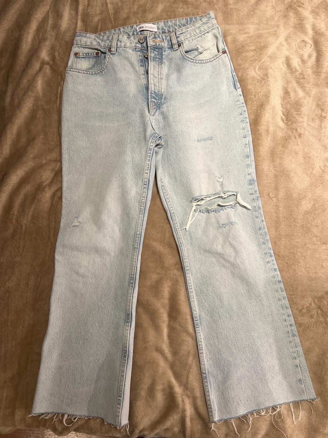 Light blue denim jeans with knee rips and frayed hem, placed on a brown surface.