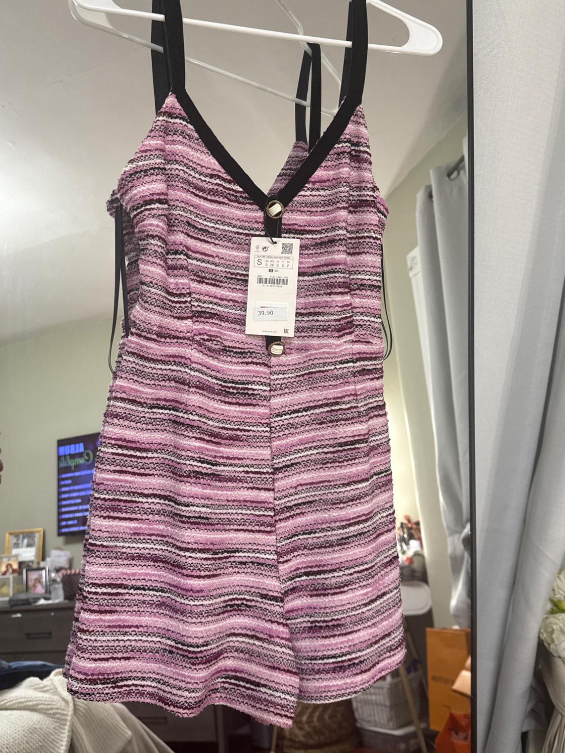 Sleeveless short black dress with horizontal striped print in shades of pink, purple, and black, hanging on a white hanger. Price: 39.90.