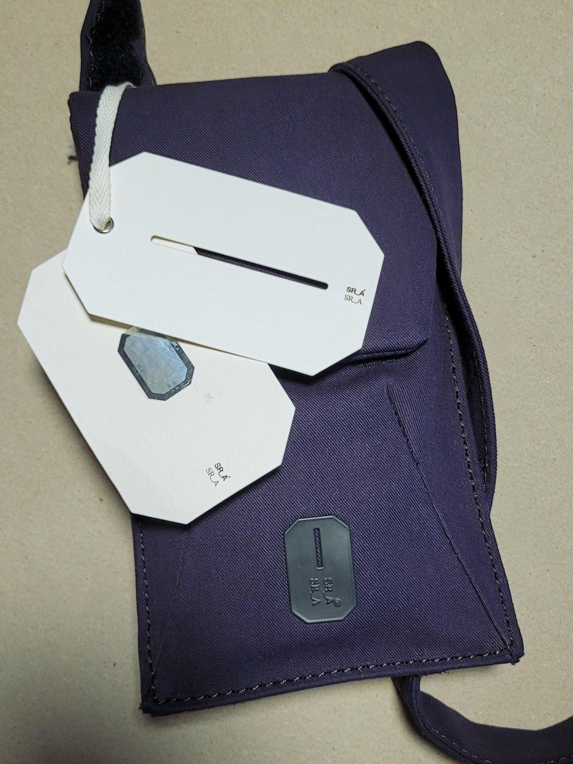 Purple handbag with white hanging tags that read "SRLA". Beige background. Minimalist and modern design.