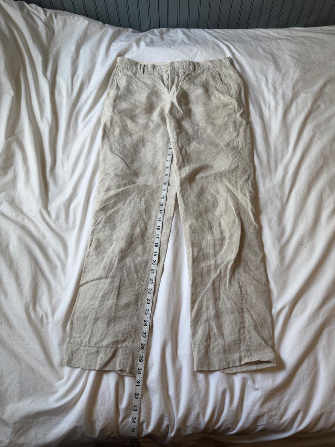 Light beige pants laid out on wrinkled white sheets. A tape measure
measures the length of the left leg.