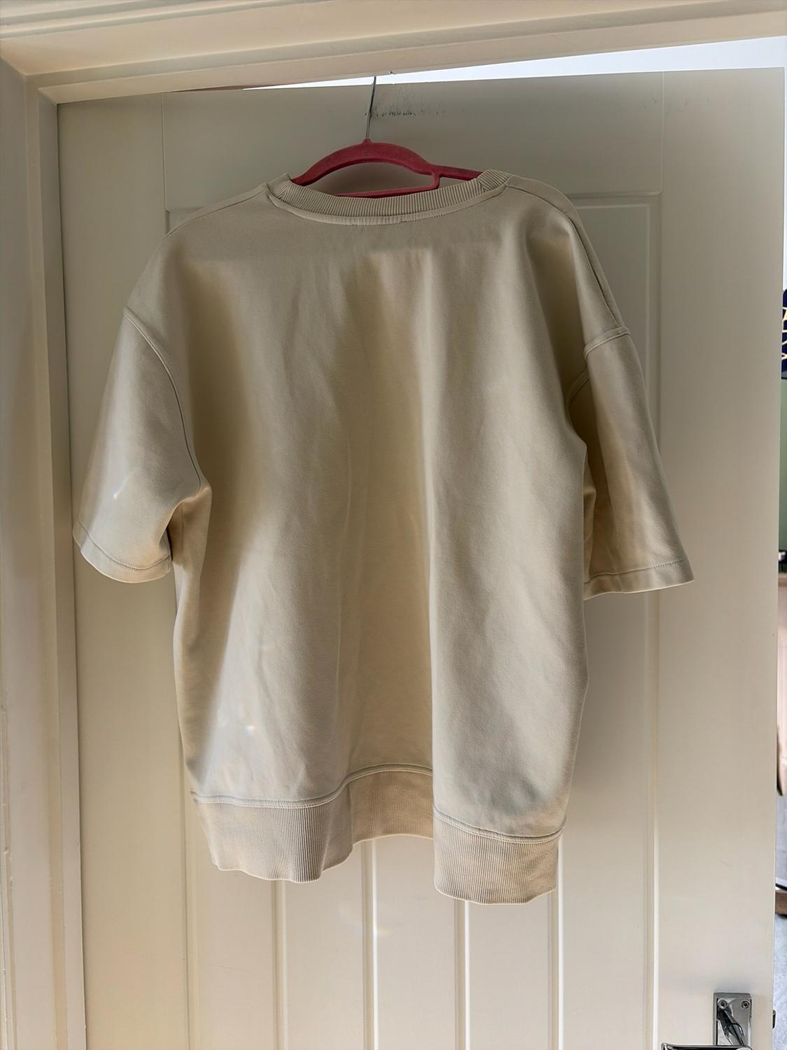 Beige short-sleeved sweatshirt hanging on a pink hanger over a white door.