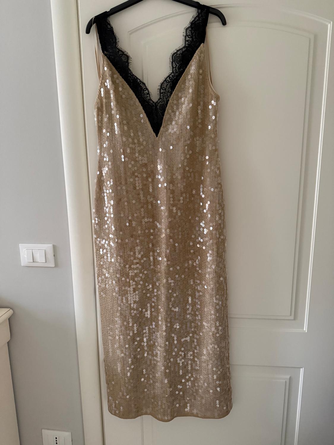 Gold sequined dress hanging on a white door, with a V-neckline and black lace straps.