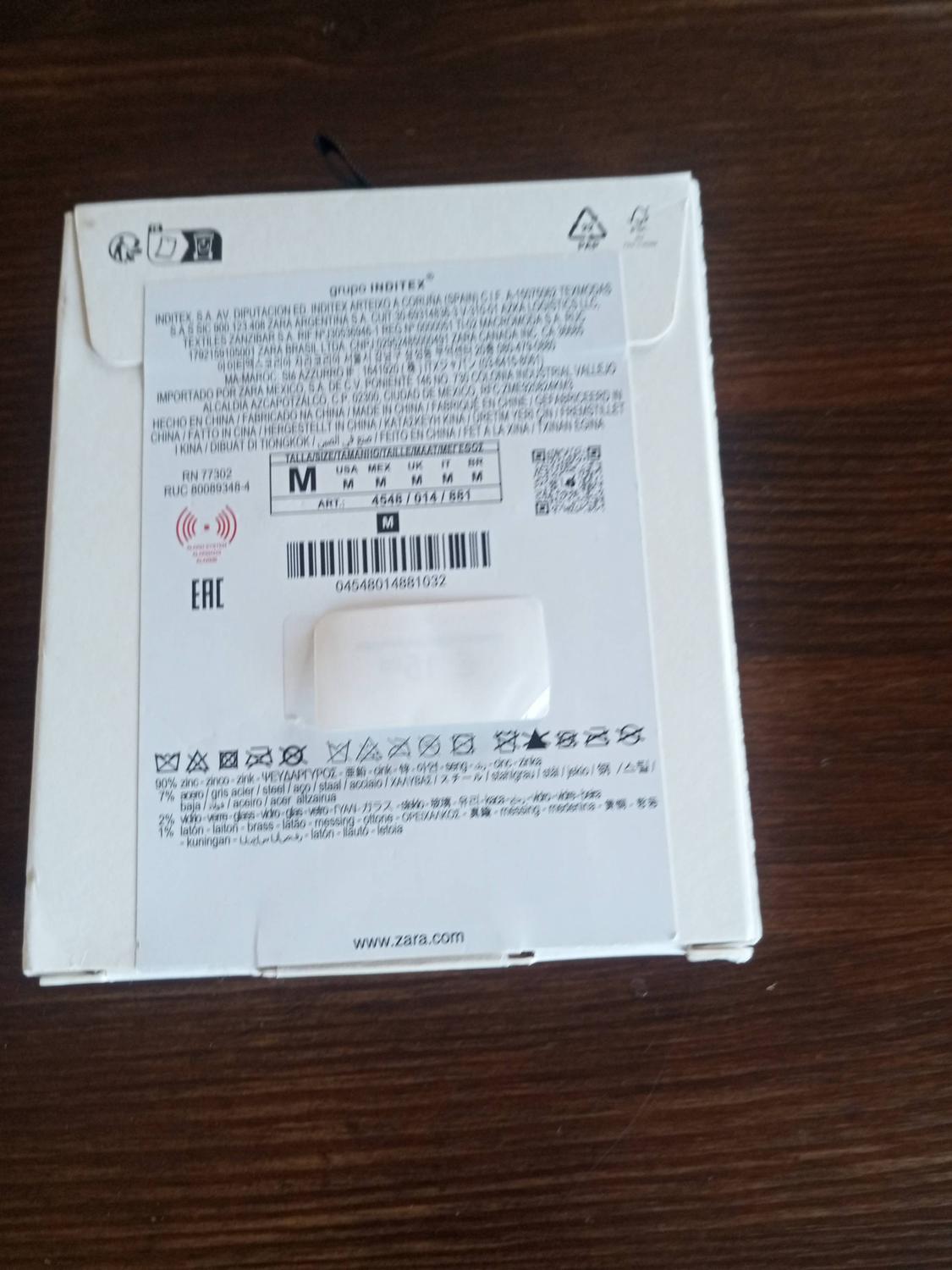White Zara box on a wooden table, with product information labels, barcodes and care symbols.