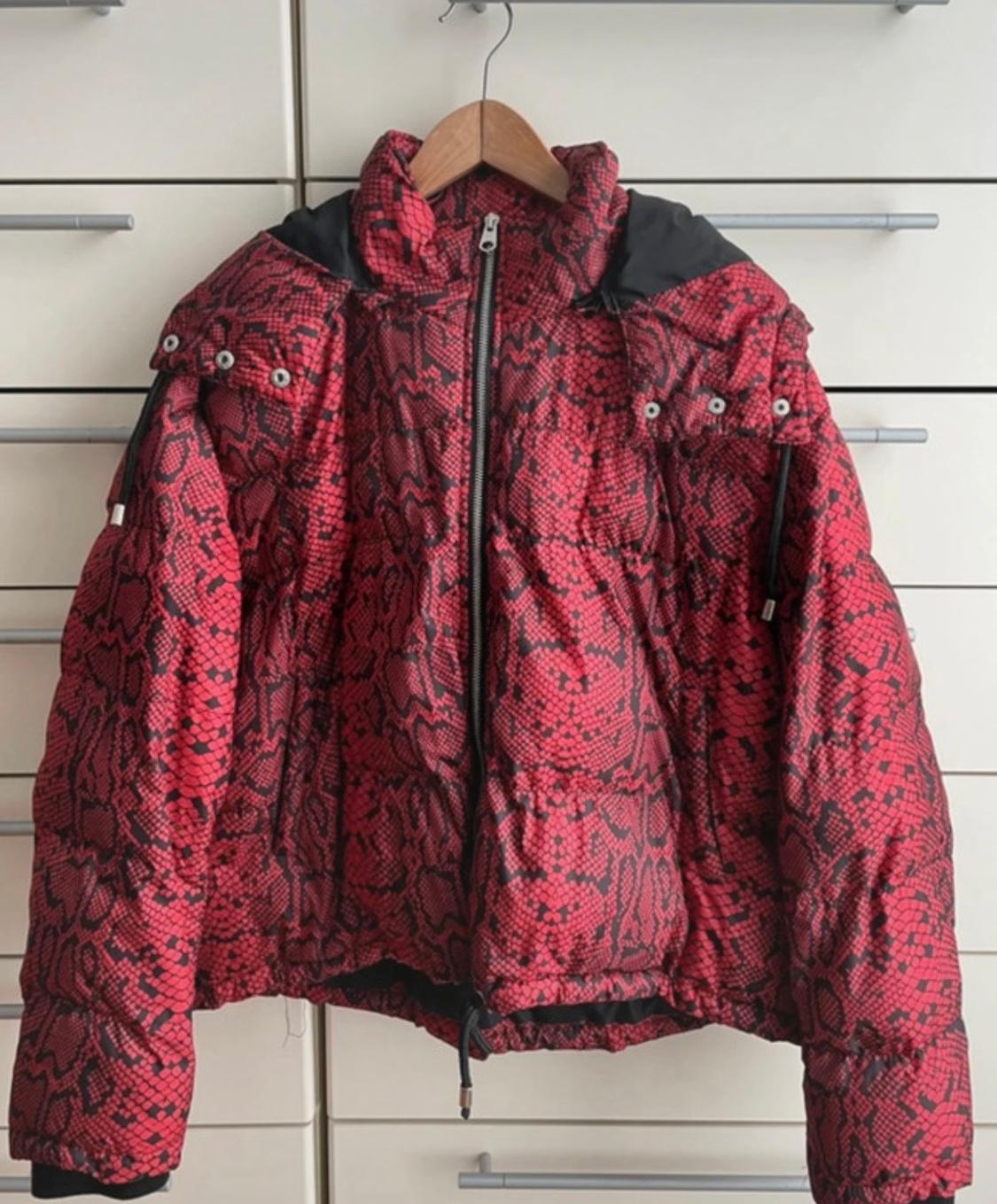 Red padded jacket with a snake print, hung on a wooden hanger in front of a background of white drawers.