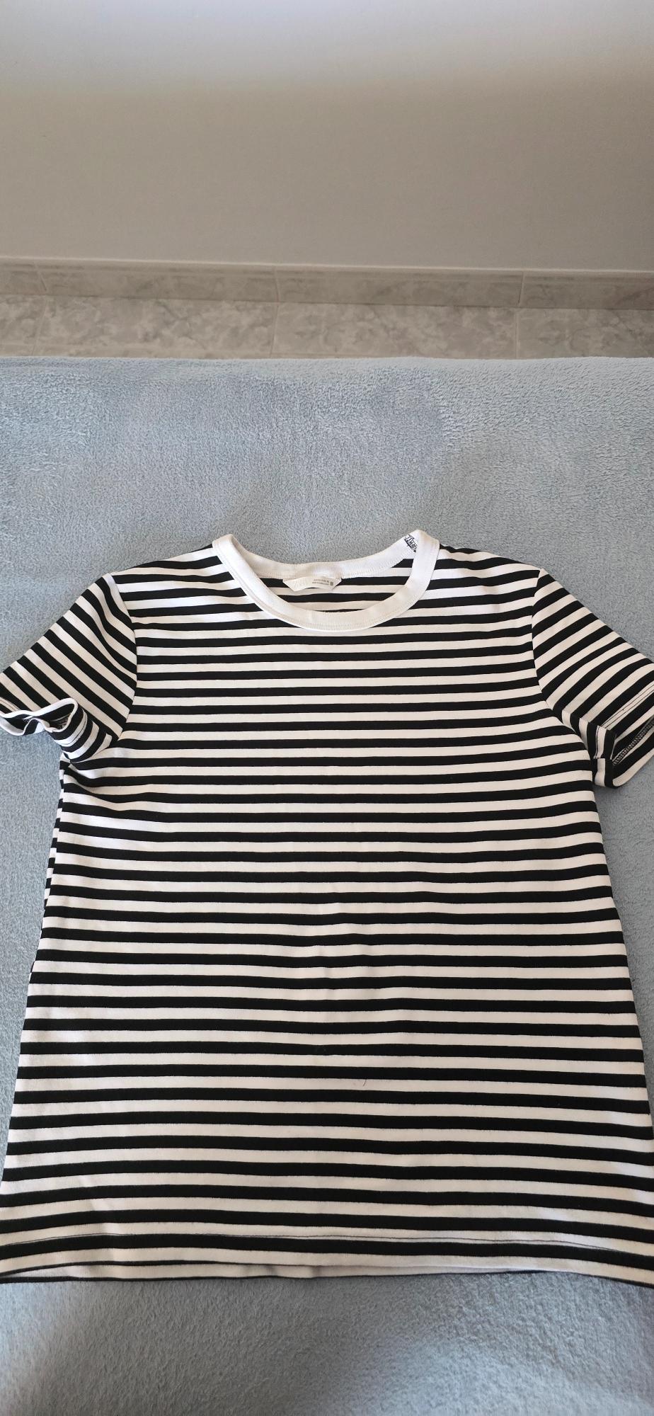 White and black horizontal striped T-shirt on a light blue surface. White wall background and tiled floor.