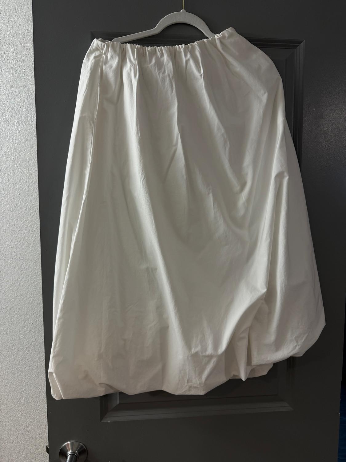 White skirt hanging on a hanger over a grey door. The fabric is lightweight and has a loose, flowing design.