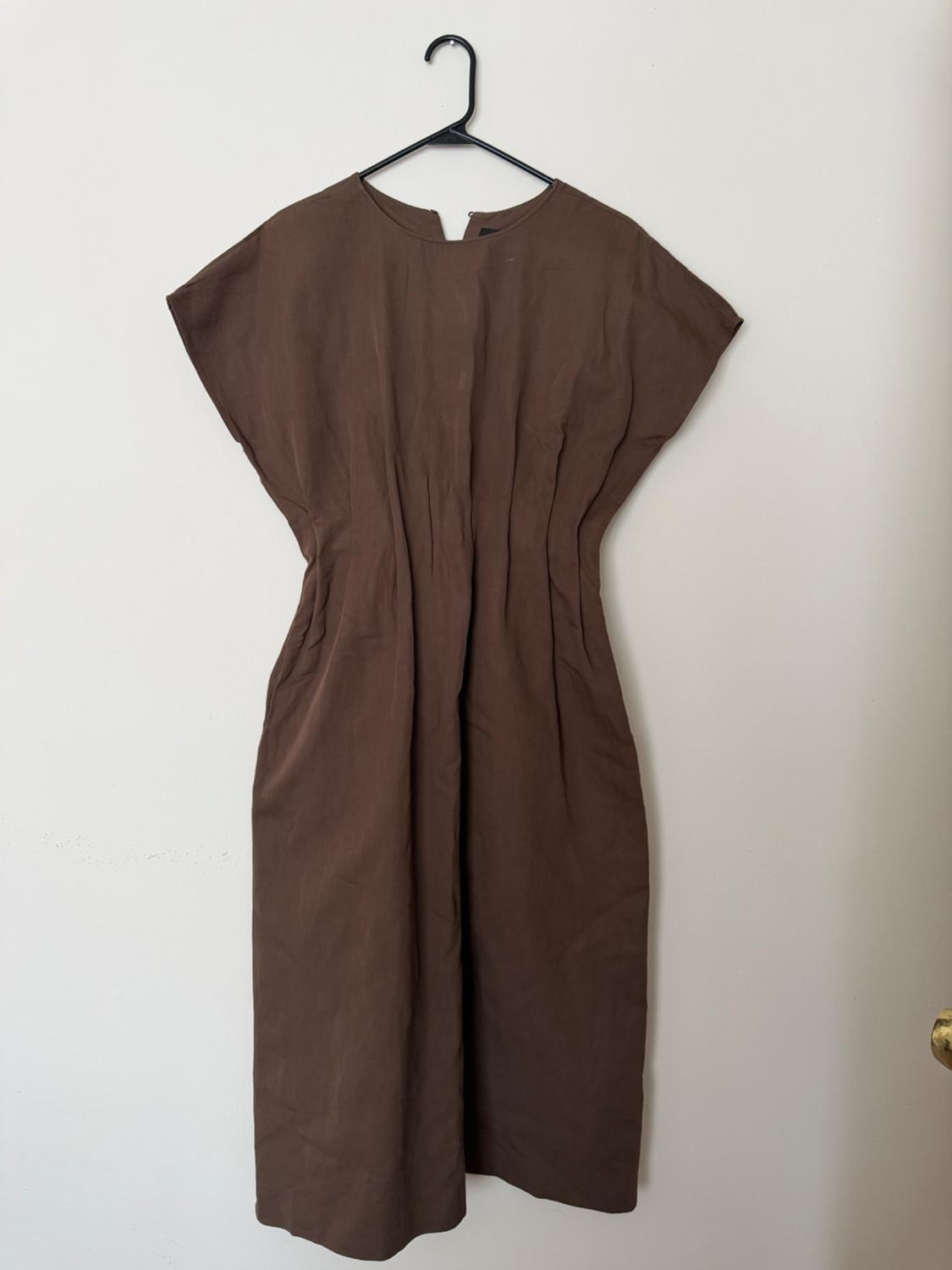 Short-sleeved brown dress hanging on a black hanger against a white wall. Simple and elegant design.