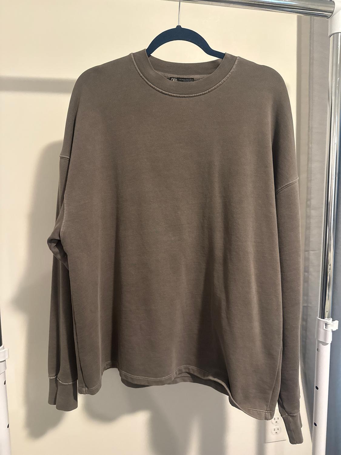 Brown long-sleeved sweatshirt hanging on a blue hanger against a white background. Casual and relaxed style.