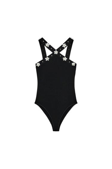 Front view of a black halter-neck bodysuit with criss-cross straps adorned with white flowers. Snap button closure at the bottom.