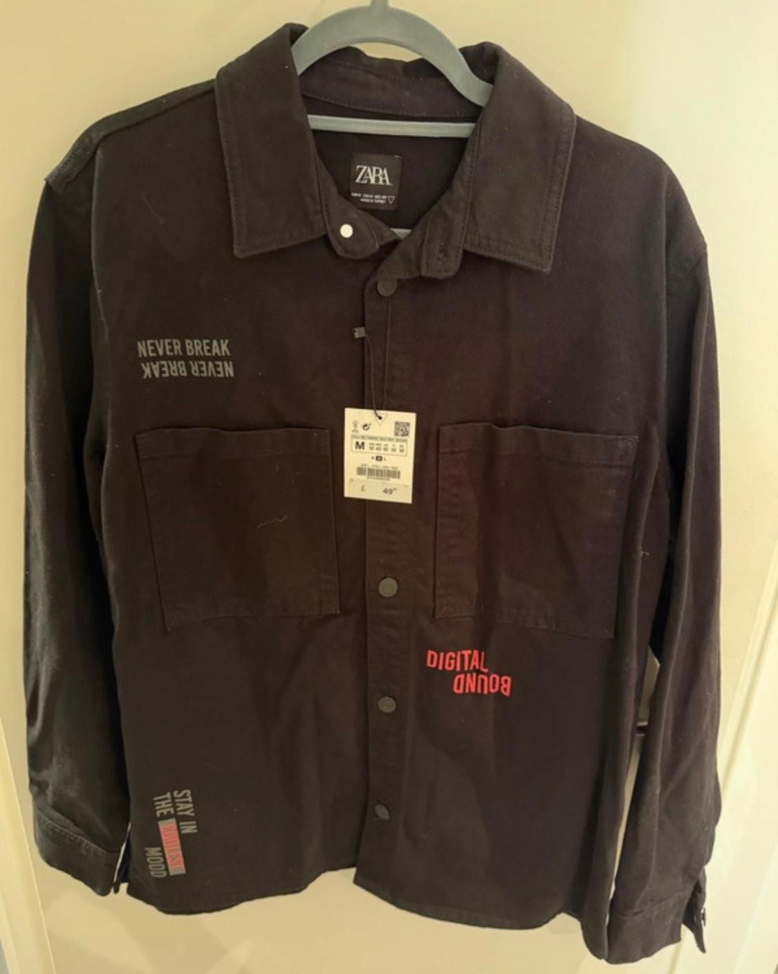 Long-sleeved black shirt on a hanger with pockets and text: ZARA, NEVER BREAK, DIGITAL BOUND, STAY IN THE COOLEST MOOD.