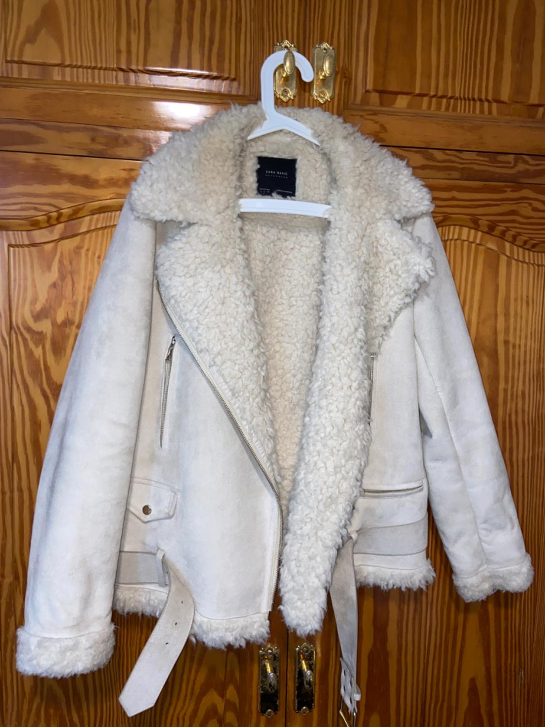 Front view of a white jacket with a sheepskin lining, front zip, side pockets and a belt.