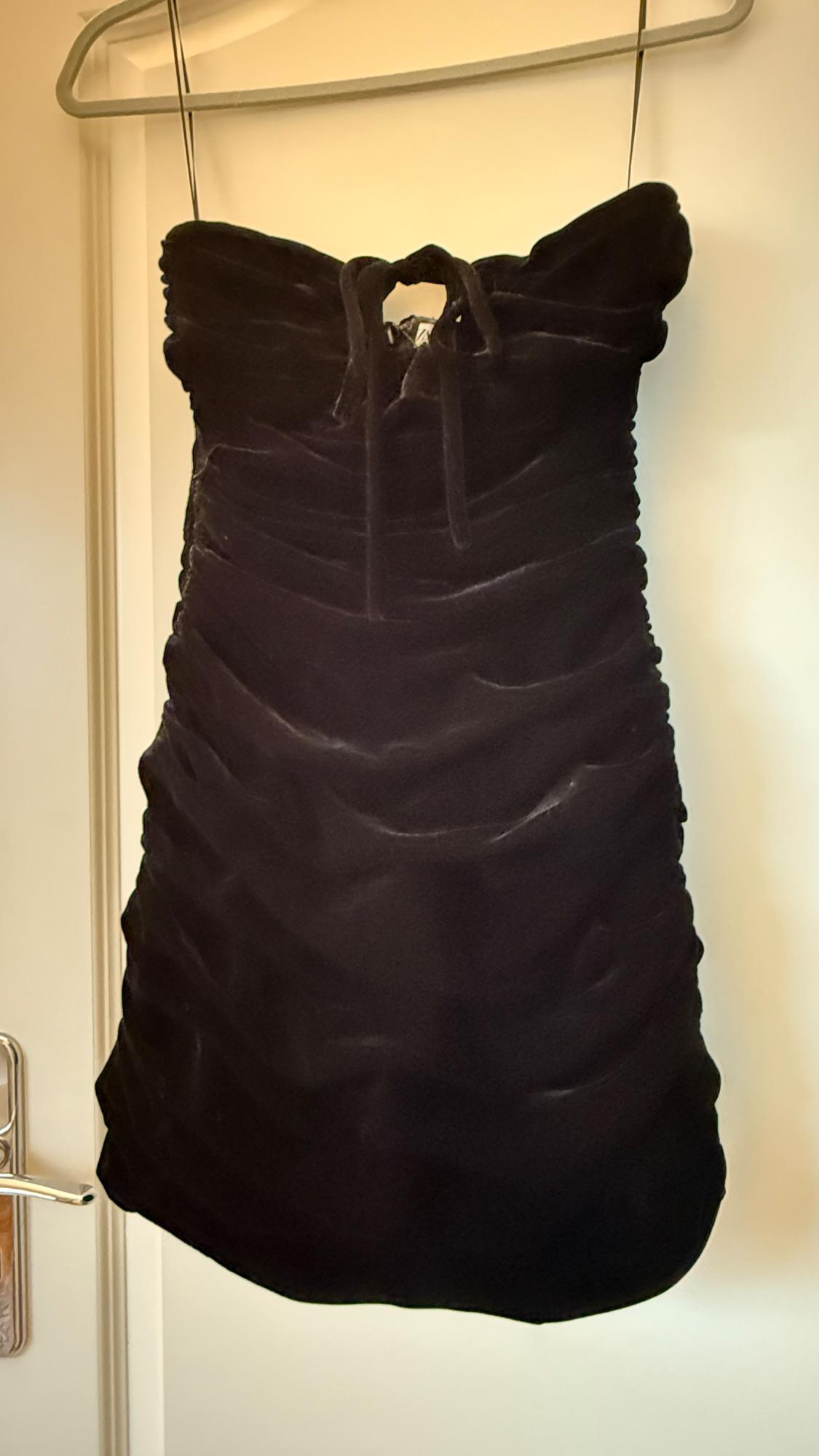 Black strapless dress hanging on a hanger, with ruching and bow on the neckline, on a light background.