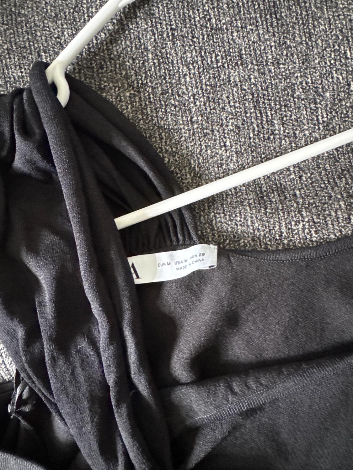 Black garment on a white hanger over gray carpet. Visible label: "EUR M USA M MEX 28 MADE IN CHINA".