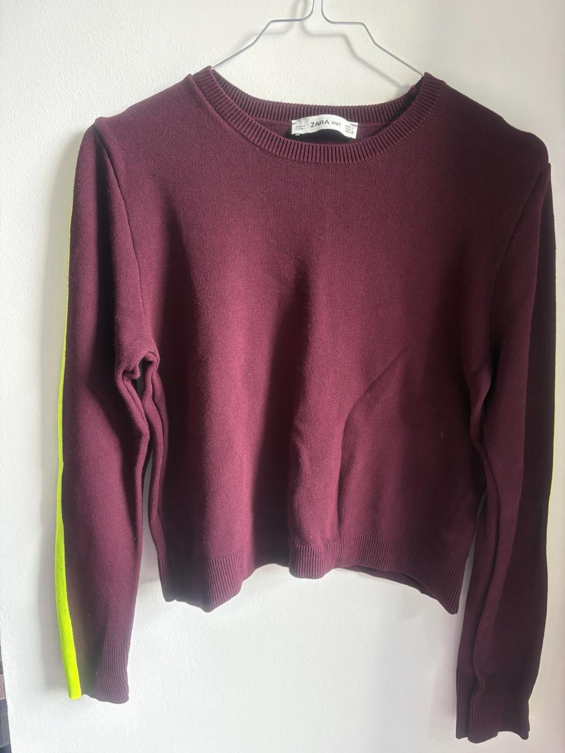 Maroon knitted jumper hanging on a hanger. It features a round neck, long sleeves with a neon yellow side stripe and a ZARA KNIT label.