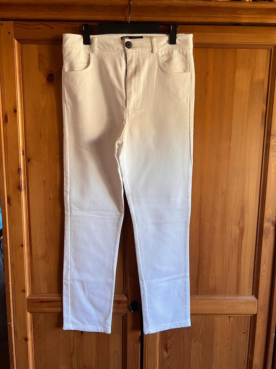 Front view of white trousers with front pockets and button fastening.