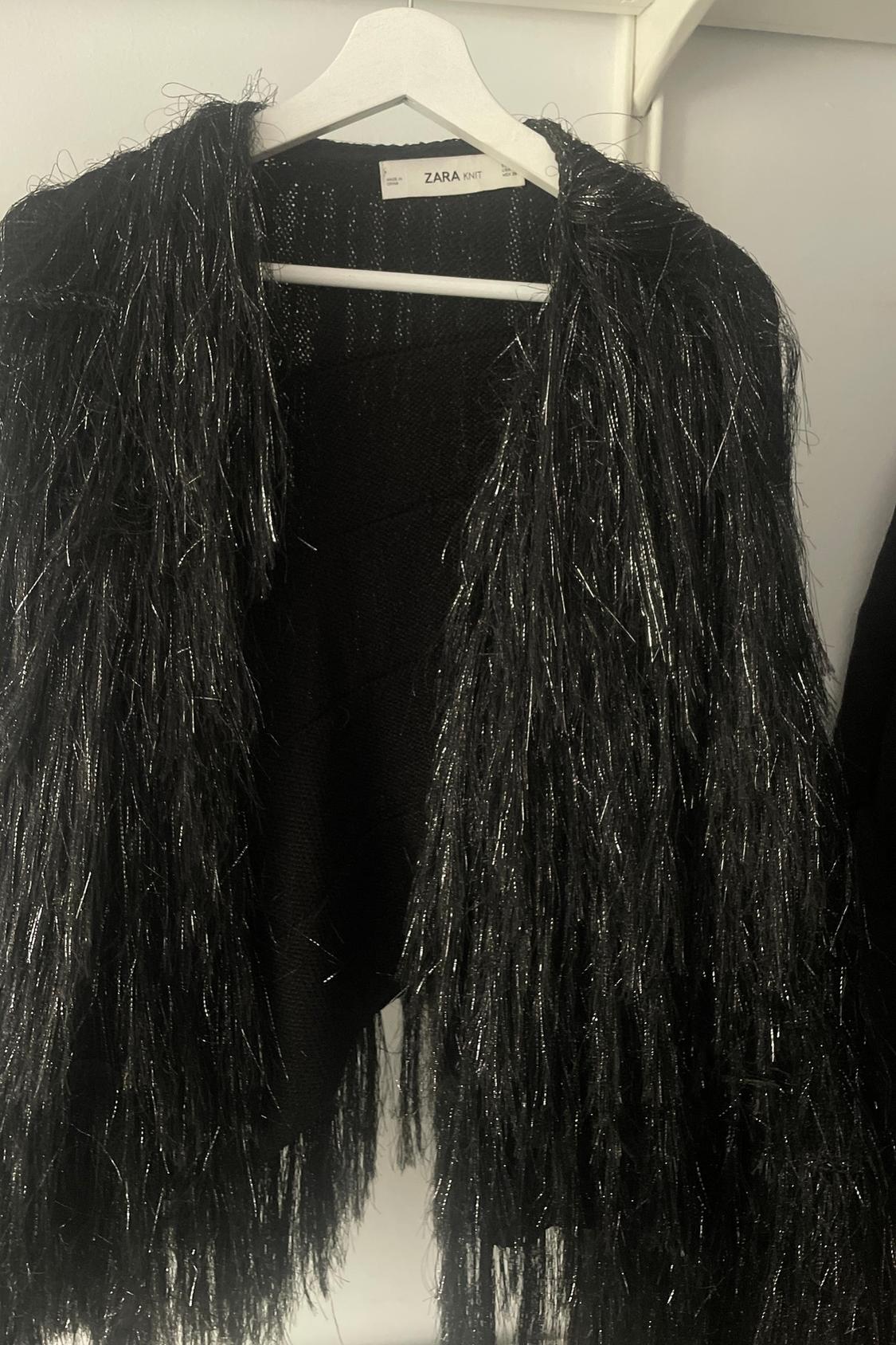 Front view of a black jacket with shiny fringe.