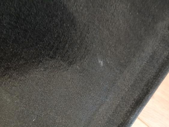Close-up of a black fabric with a velvety texture, showing a slight sheen and a small white spot in the centre.