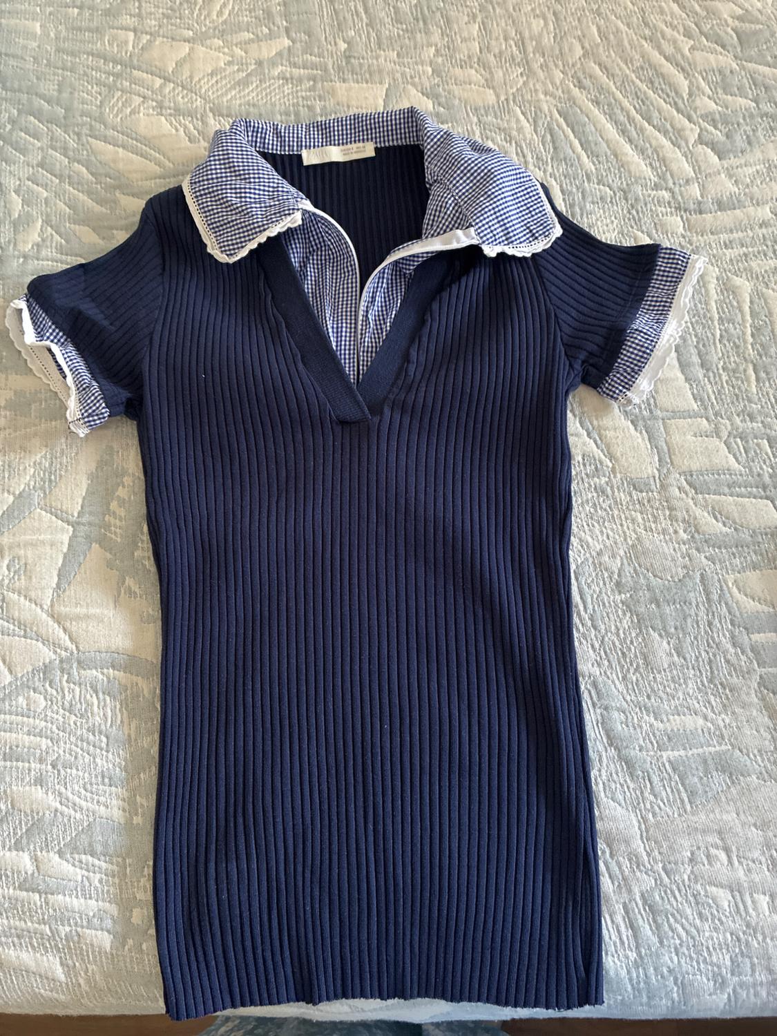 Navy blue ribbed-knit top with a collar and cuffs featuring blue and white checks with lace, against a textured background.