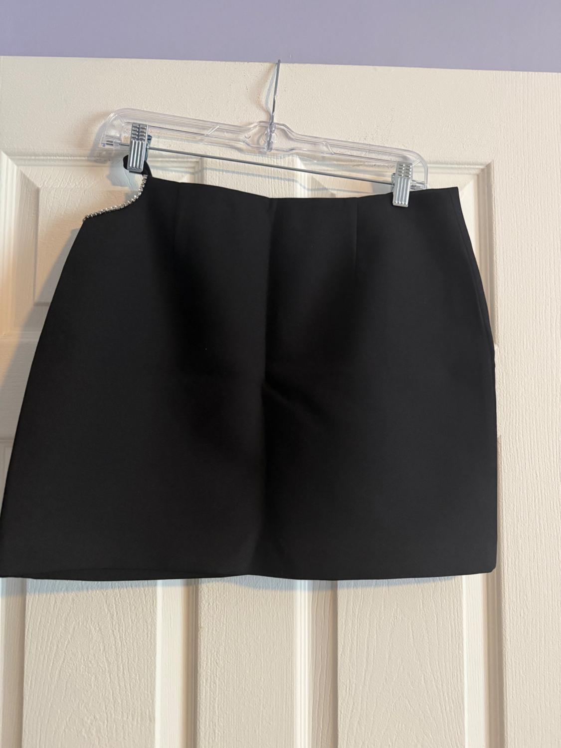 Black skirt hanging on a clear hanger over a white door. The skirt has a simple and elegant design.