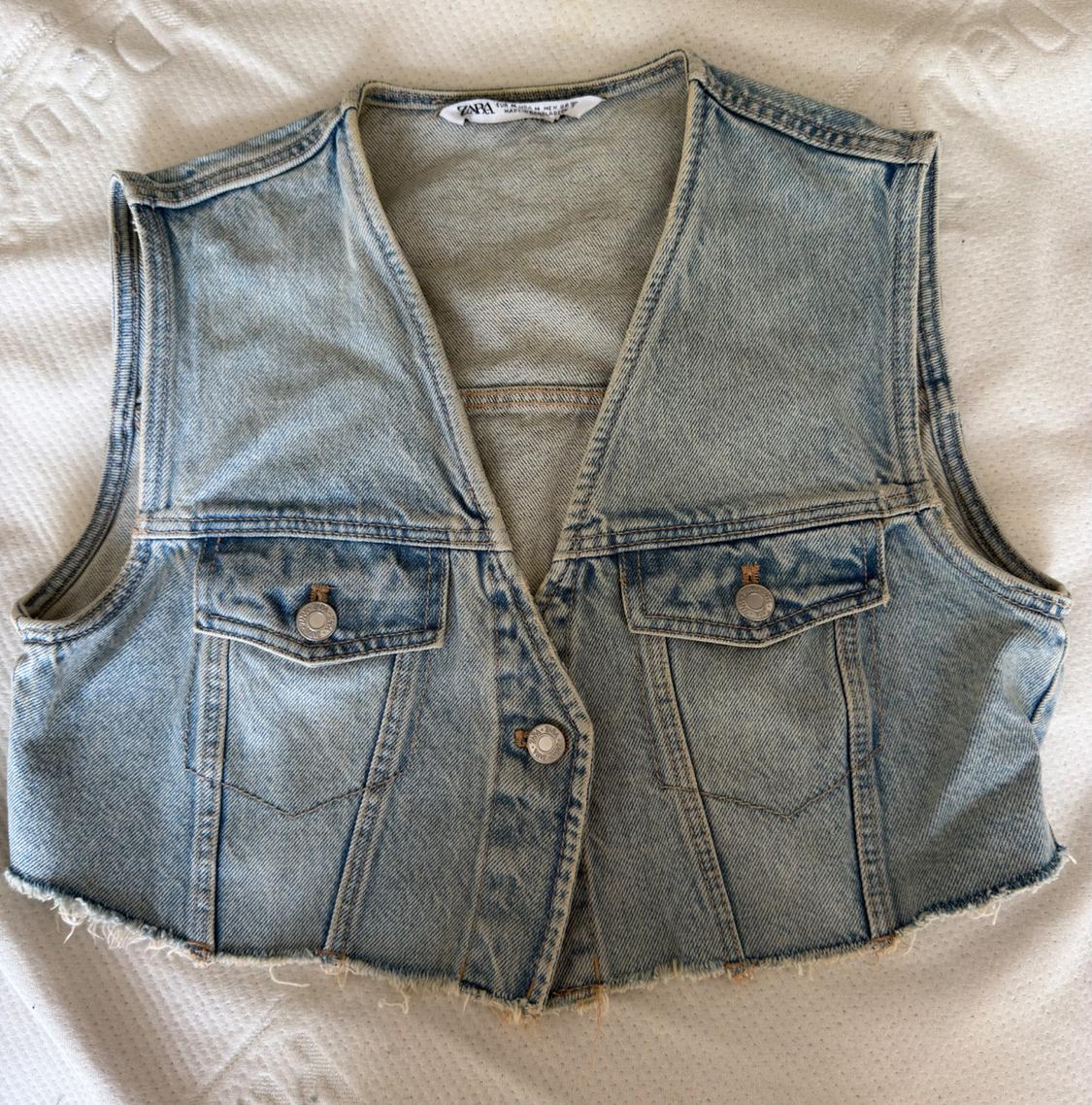 Light blue denim waistcoat with a V-neck, buttons, pockets, and a frayed hem on a white surface. Text: ZARA.