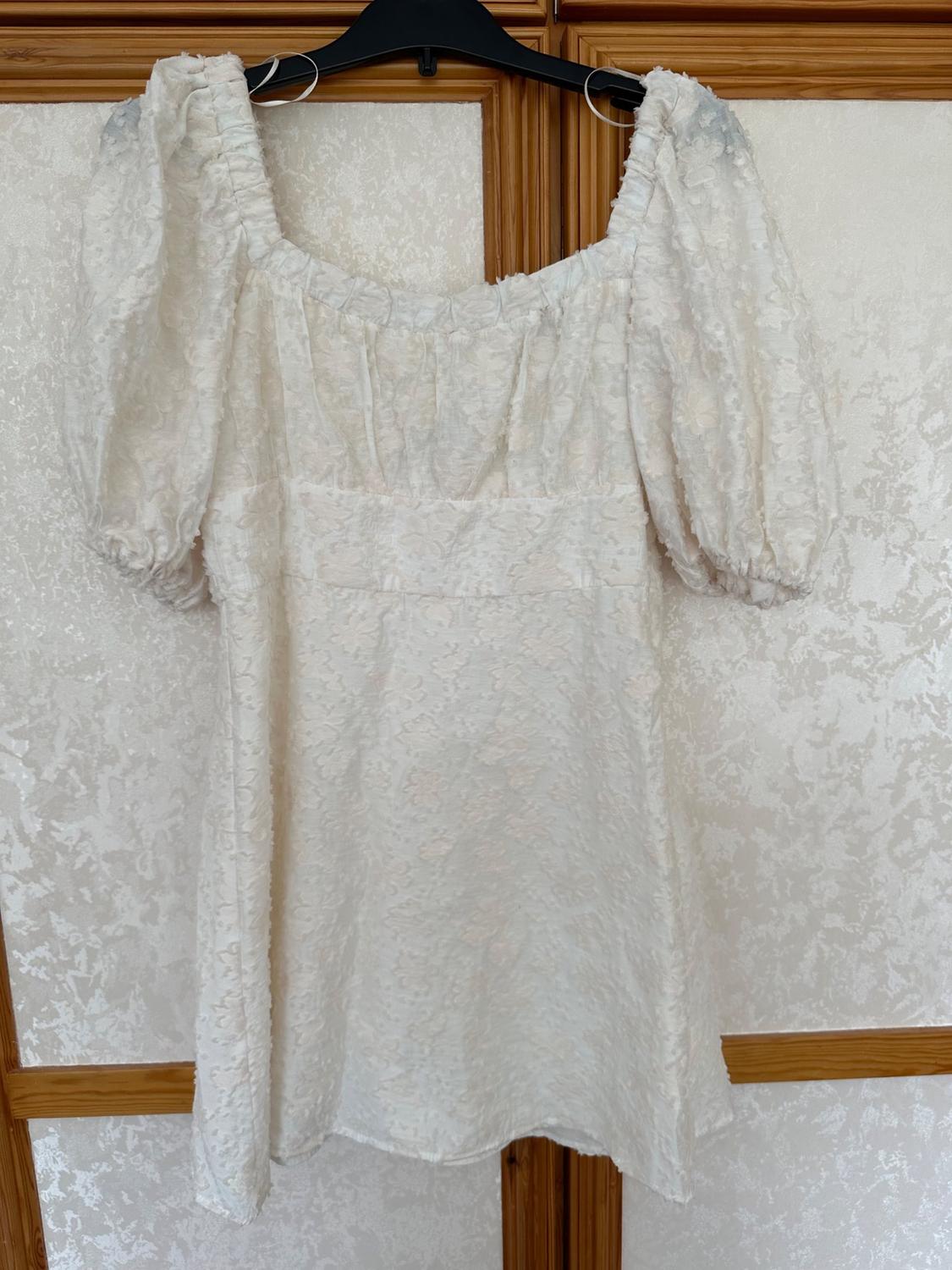 Front view of a white dress with puff sleeves and a square neckline.