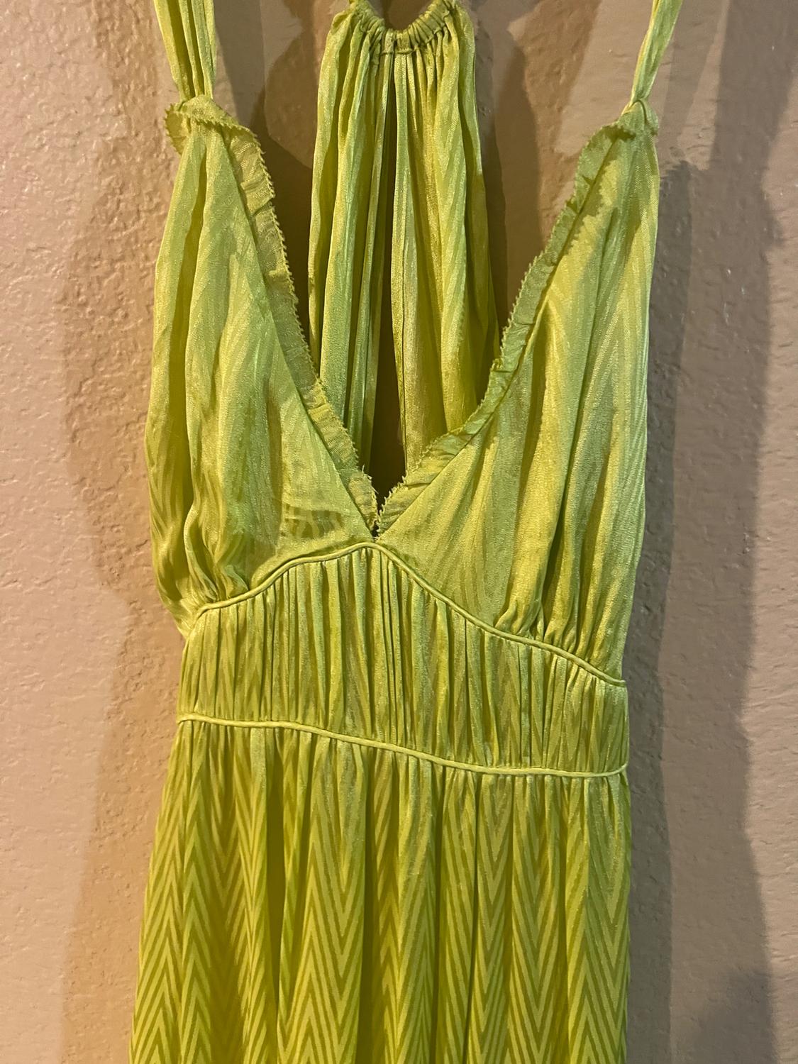 Light green dress with spaghetti straps and a V-neck, pleated fabric and chevron pattern, hanging on a beige wall.