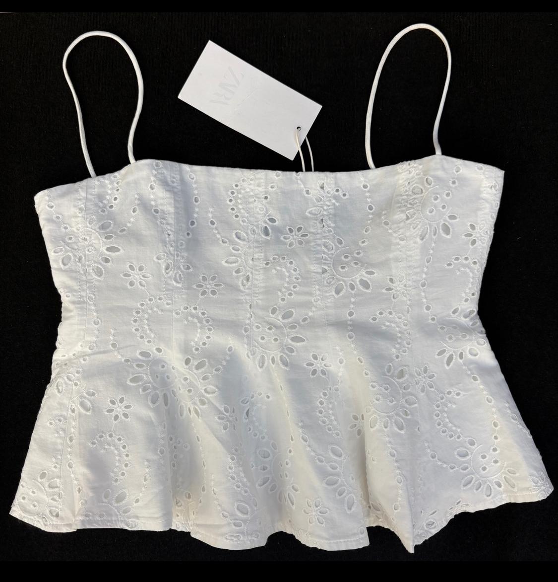 White camisole top with floral embroidery on a black background. White tag hanging from the left strap.