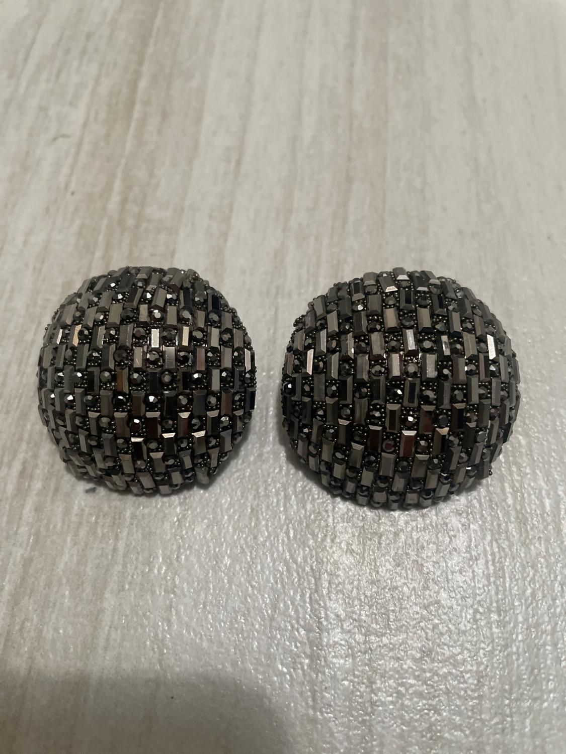 Two round earrings with a mosaic design in dark and bright tones on a light wooden surface.