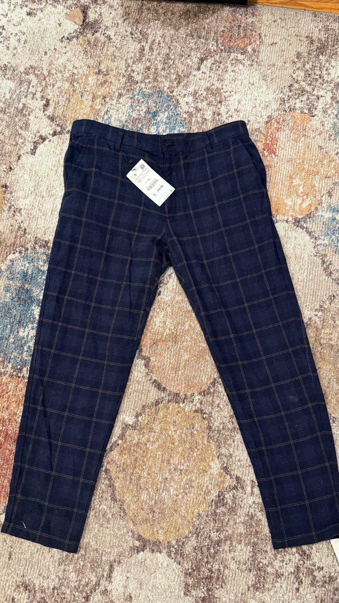 Dark blue pants with a plaid pattern on a textured rug. Visible tag with barcode and price.
