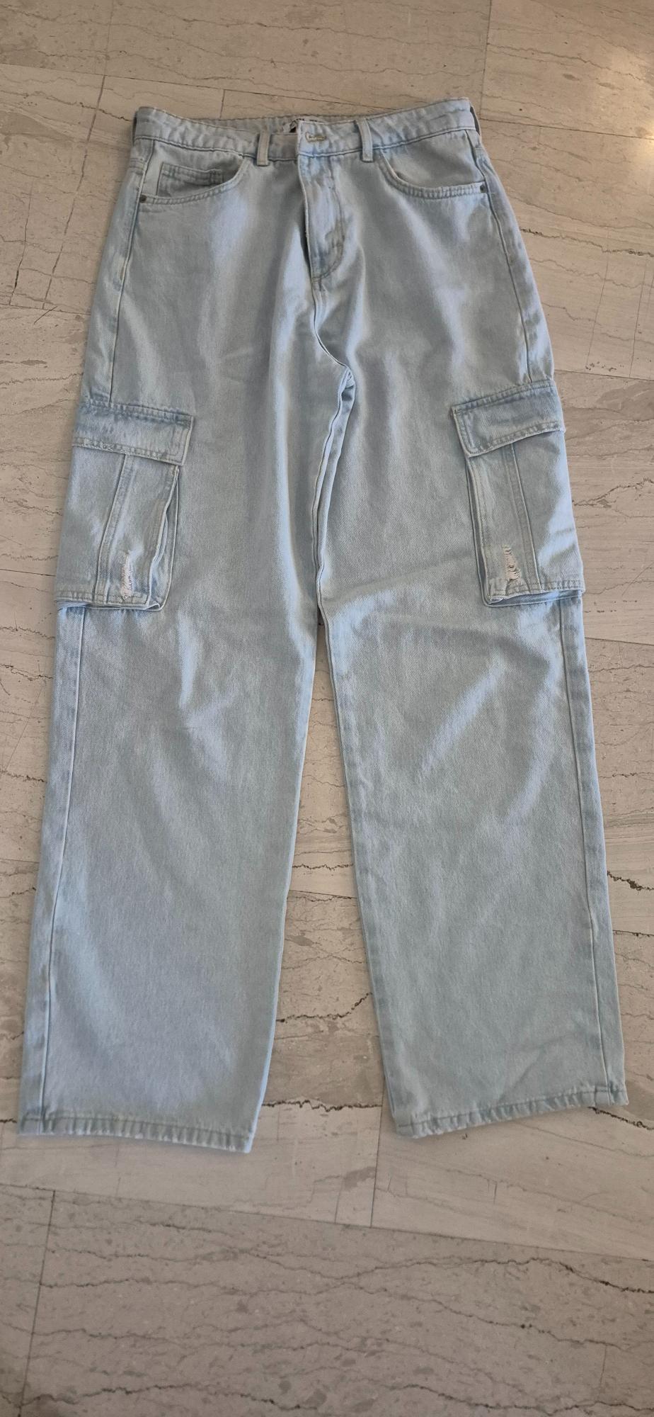 Light blue denim cargo trousers with large side pockets, placed on a beige marble floor.