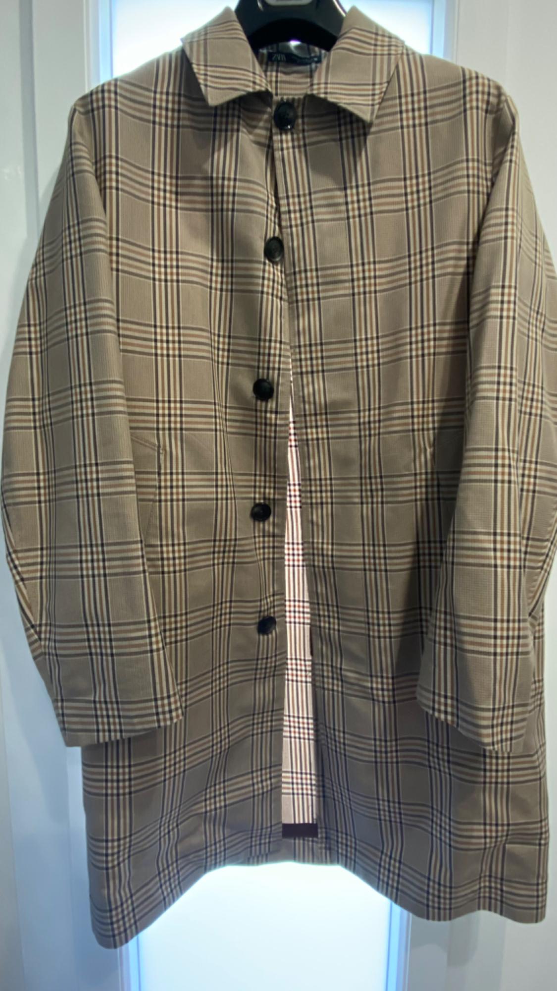 Brown and black plaid coat with dark buttons, hanging on a hanger against a lit white background.