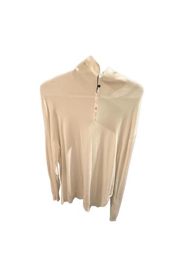White long-sleeve ribbed turtleneck sweater with a tag, on a white background.