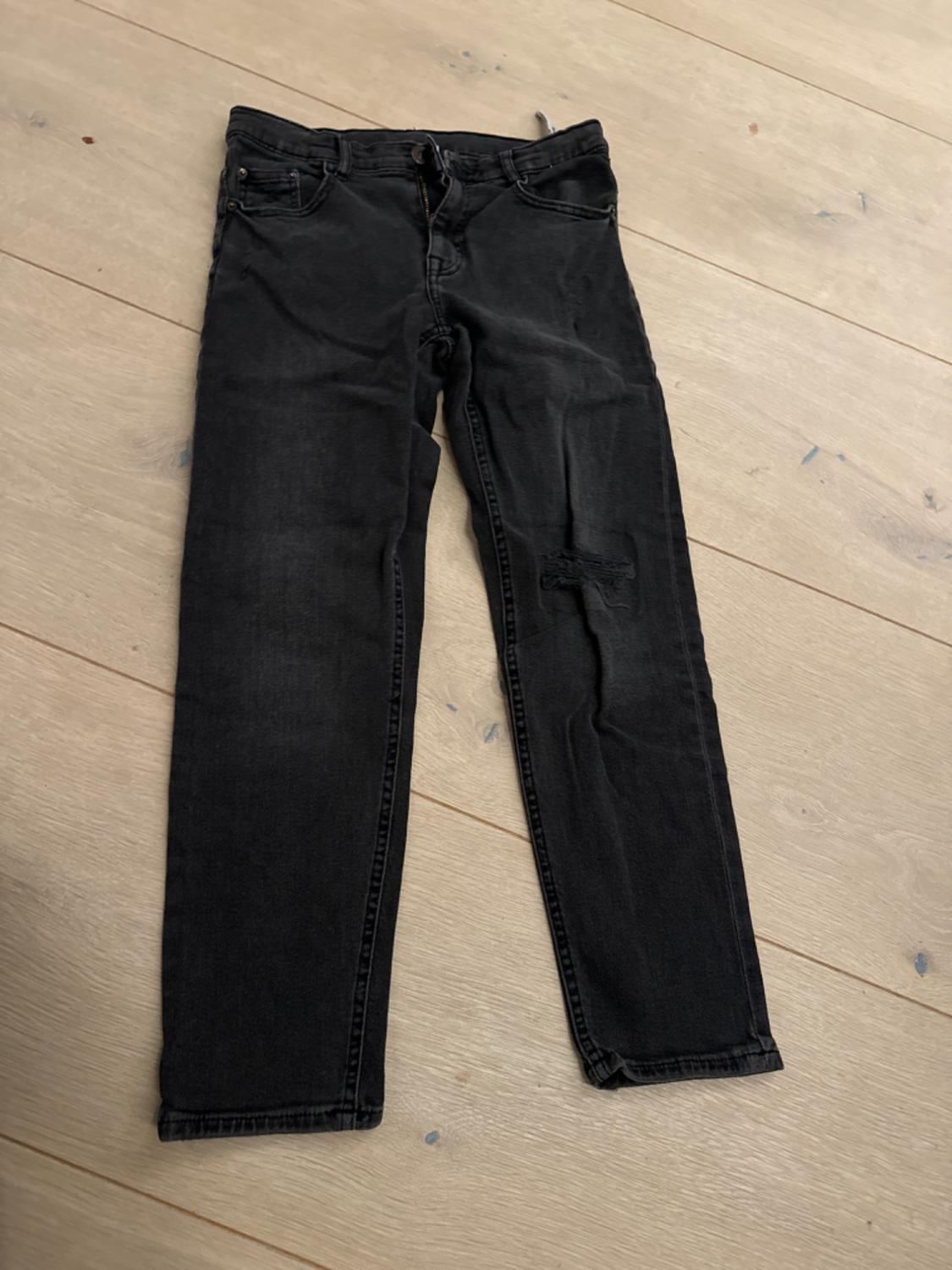 Black denim jeans on a light wooden floor. Classic five-pocket design with button and zip fastening.