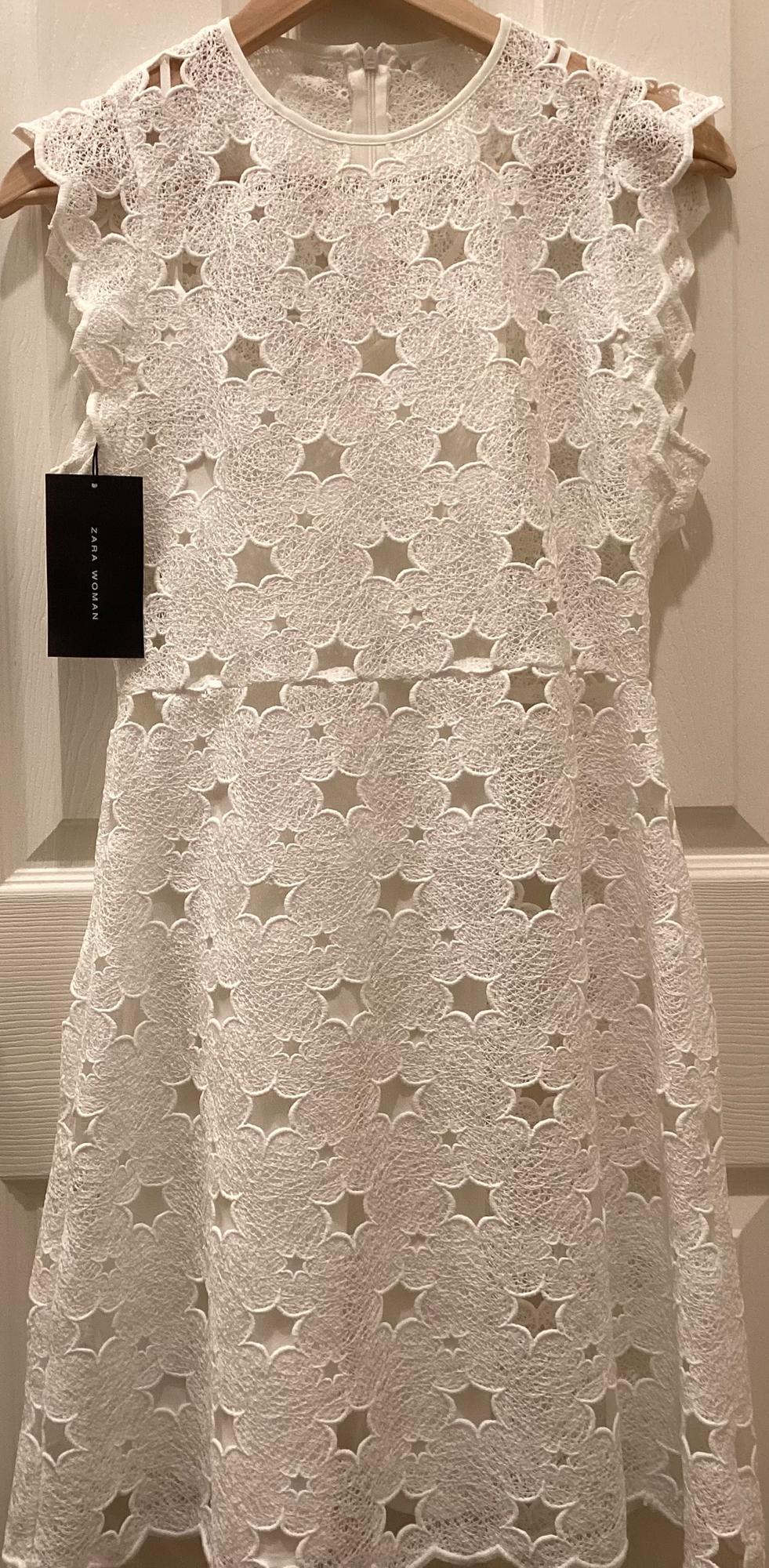 Front view of a white dress with floral lace, sleeveless and with a back closure.