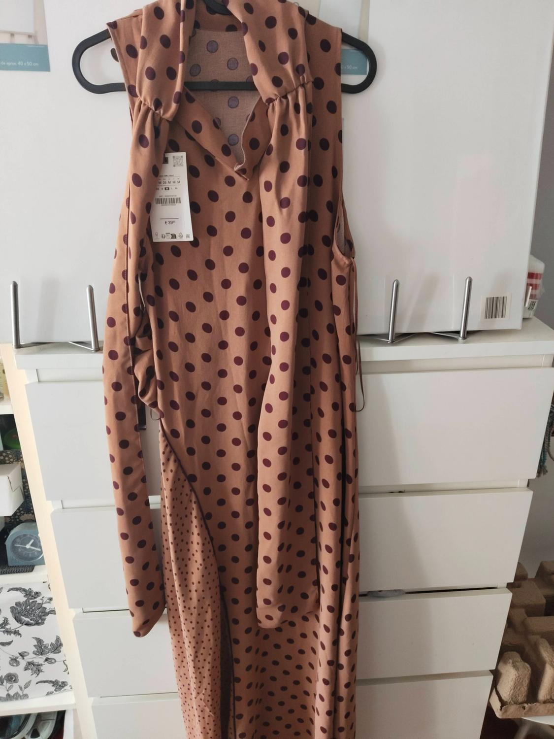 Brown polka dot dress hanging on a hanger in front of a white chest of drawers. Text: approx. 40 x 50 cm, €39.