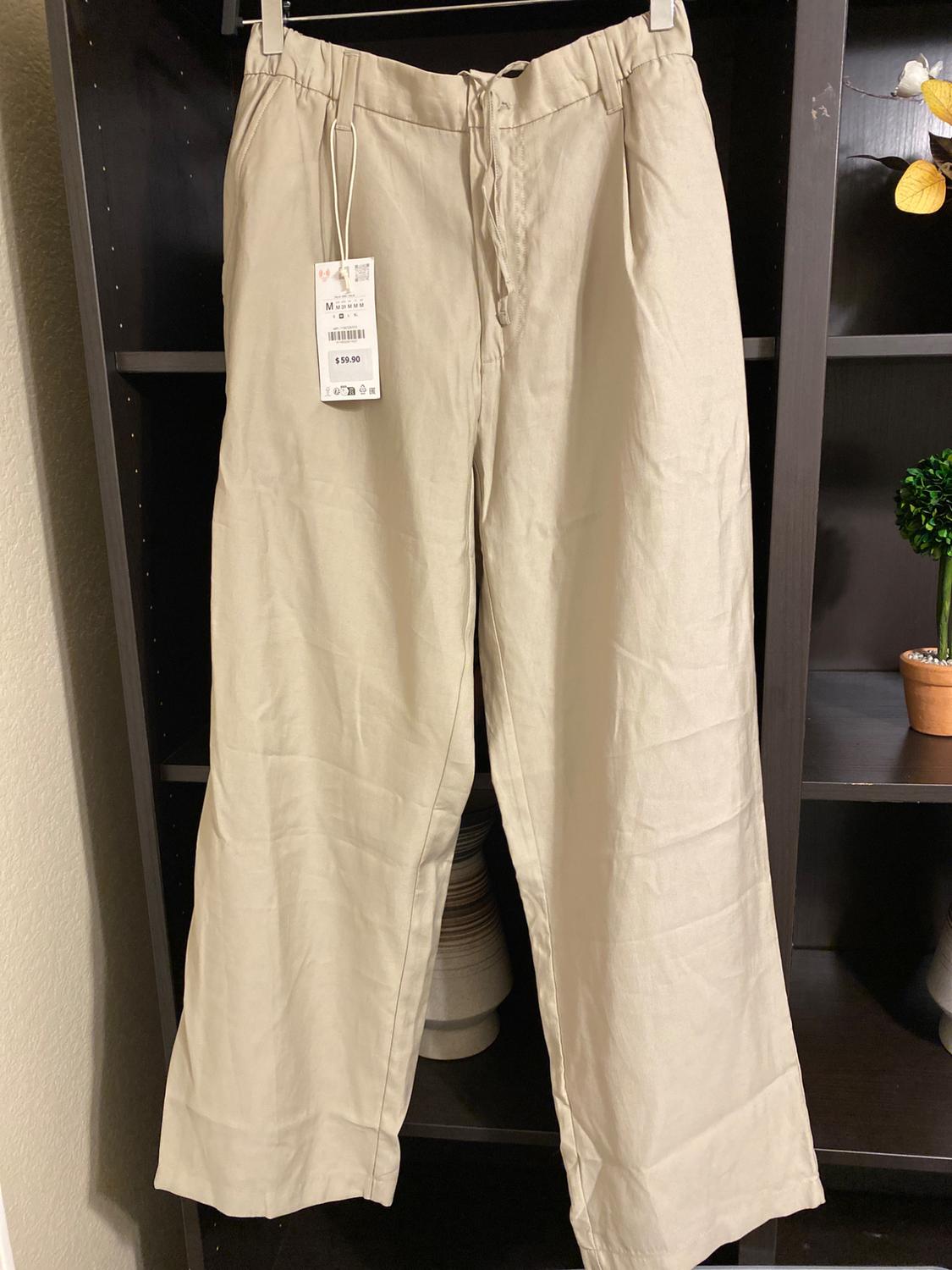 Beige trousers hanging on a dark shelf, with a price tag of $59.90. Background with plant and ceramic decoration.