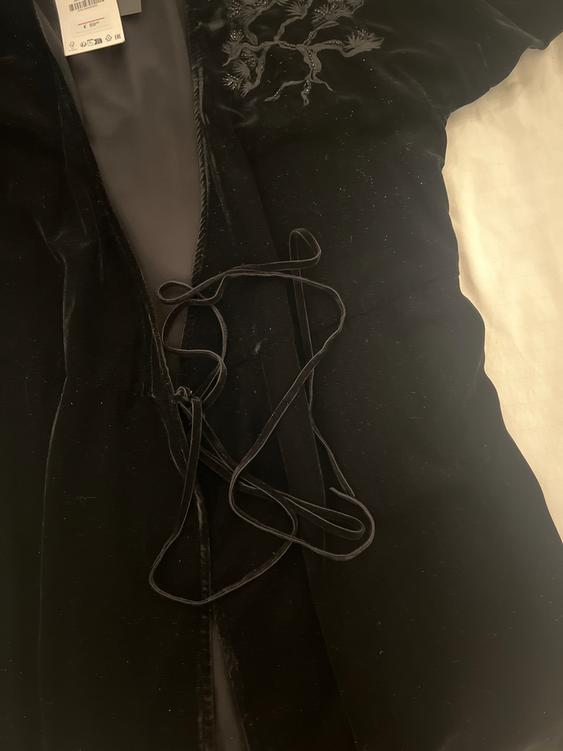 Black velvet jacket with tree embroidery on the chest. Loose ribbon and visible price tag on the inside.